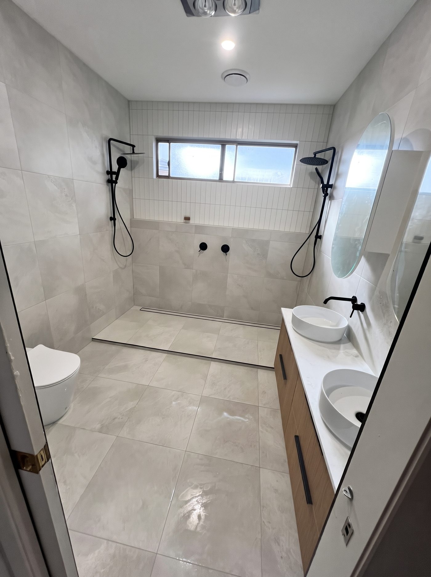 Ensuite bathroom with timber vanity, dual rain shower heads and floor-to-ceiling tiling
