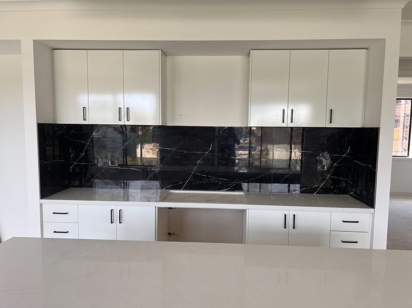 Kitchen with black stone-look tiled splashback and white cabinetry