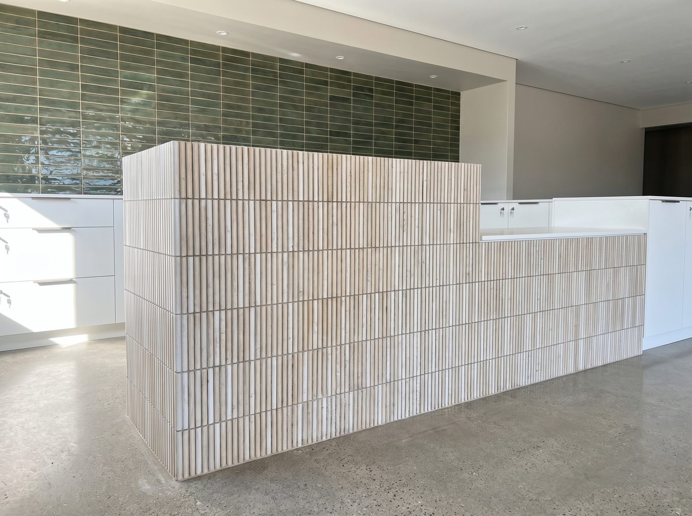 Fluted tile-clad reception desk with green brick tile feature wall