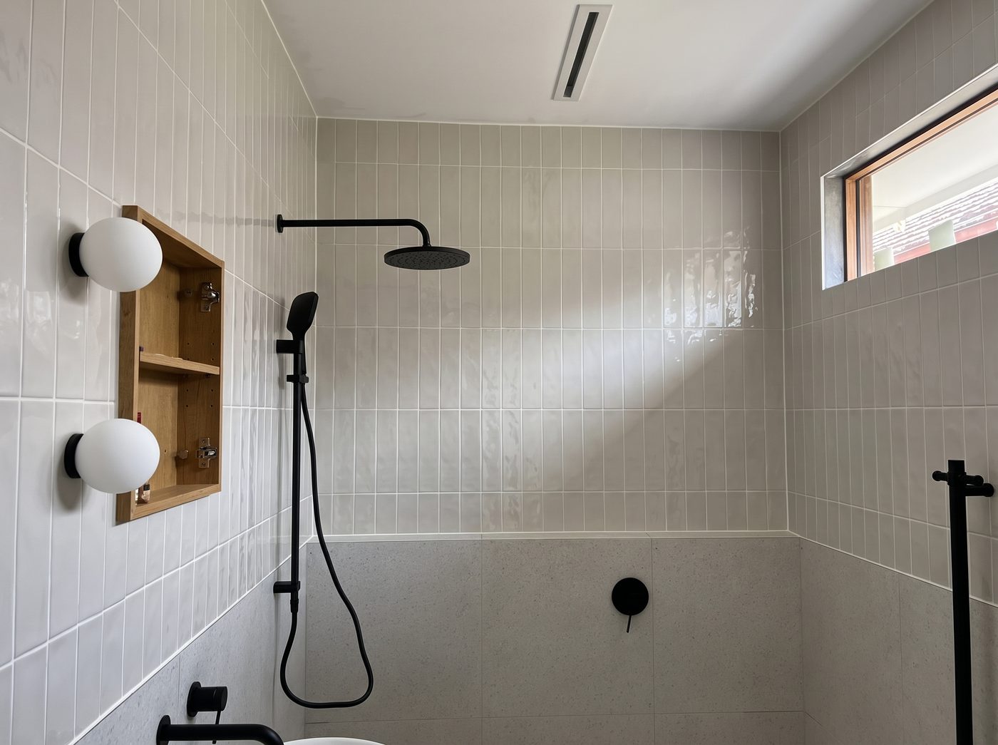 Shower tiling with black tapware and recessed timber-shelved niche